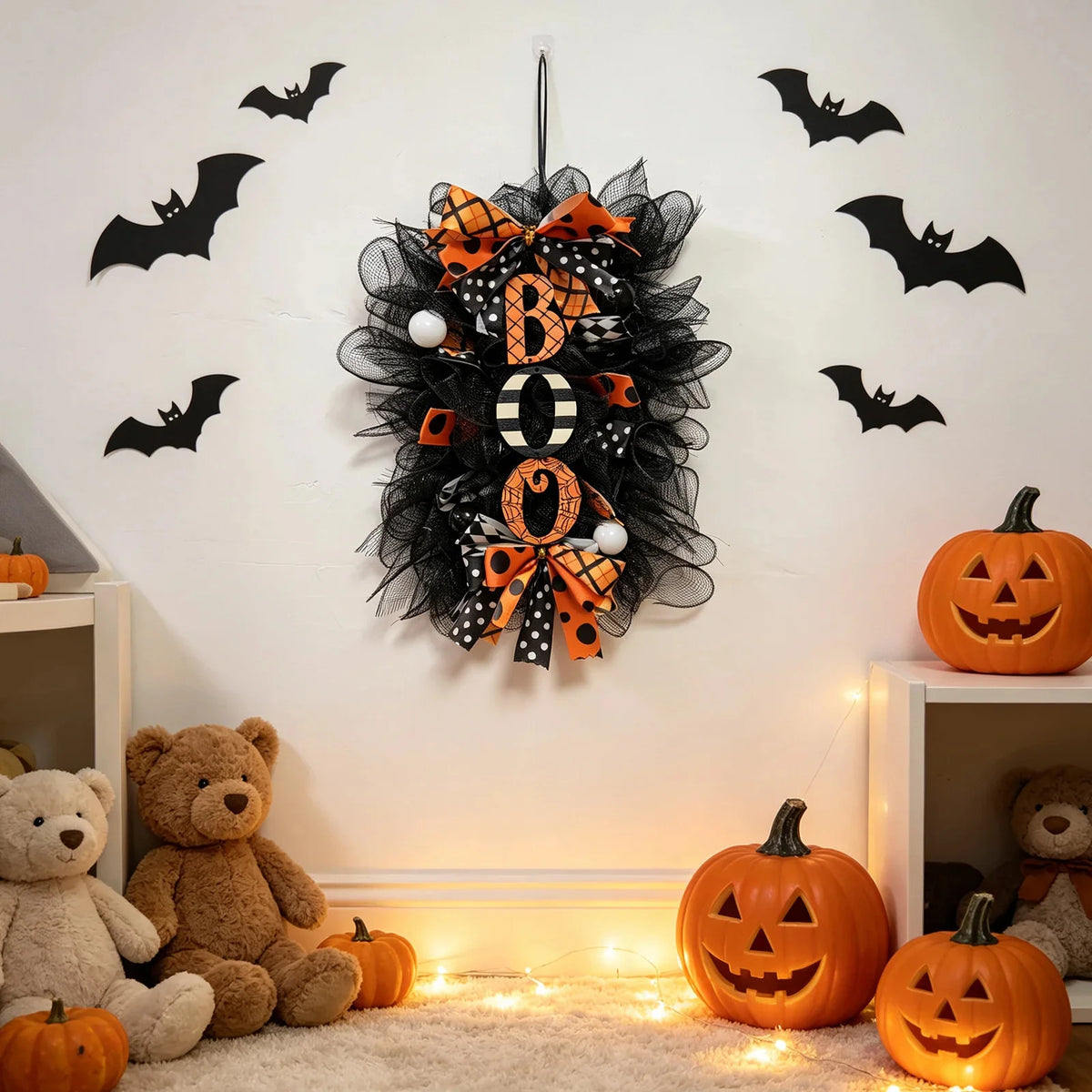 A black and orange Halloween BOO wreath with a pumpkin garland hanging on a white wall.