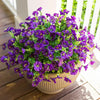 A potted arrangement of purple artificial morning glory flowers and green eucalyptus stems on a wooden deck.