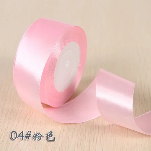 A roll of pink silk satin ribbon used for gift wrapping and craft projects.