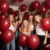 Five young women smiling while holding a cluster of burgundy red latex balloons.