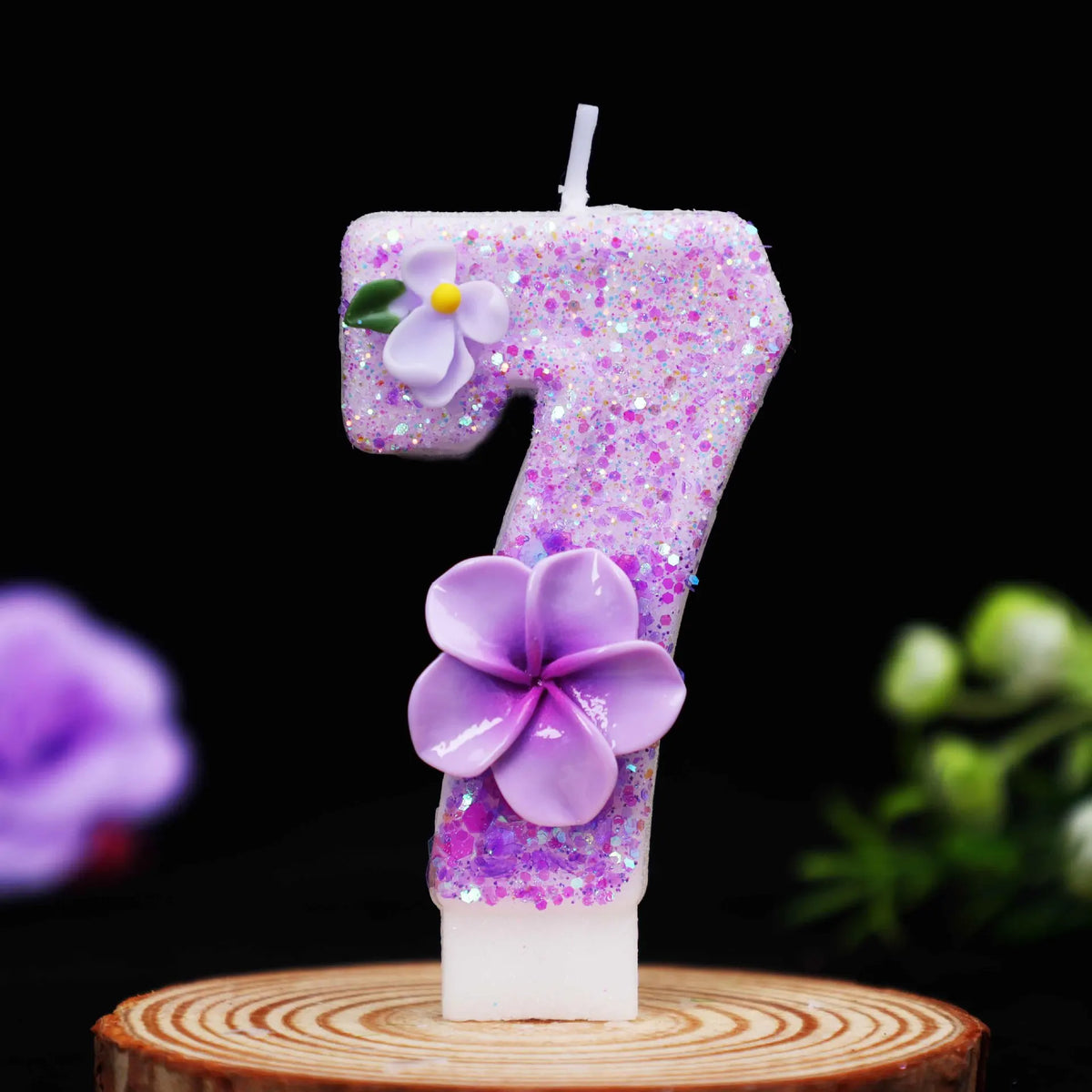 A glitter purple number seven candle decorated with a purple flower, set on a wooden surface.