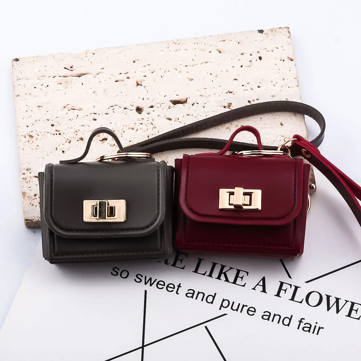 A maroon leather mini openable bag with gold hardware resting on a piece of textured paper.