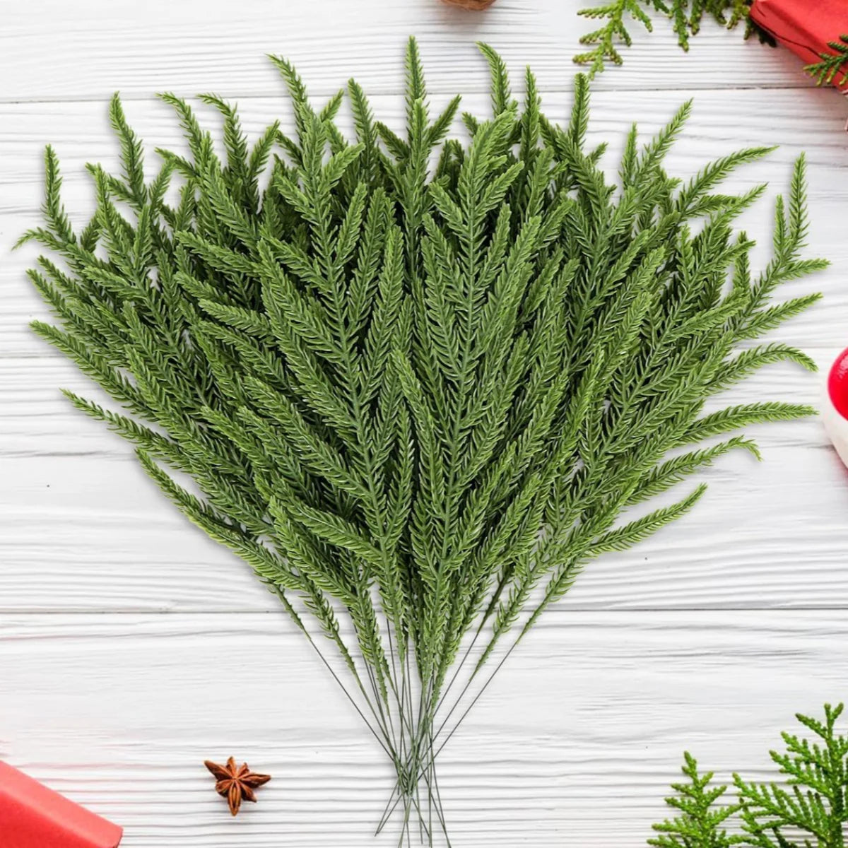 A bundle of lifelike artificial green pine branches used for holiday decoration on a white wooden surface.