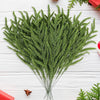 A bundle of lifelike artificial green pine branches used for holiday decoration on a white wooden surface.