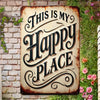 A rustic iron wall sign with carved text that reads This Is My Happy Place, set against a brick and greenery background.