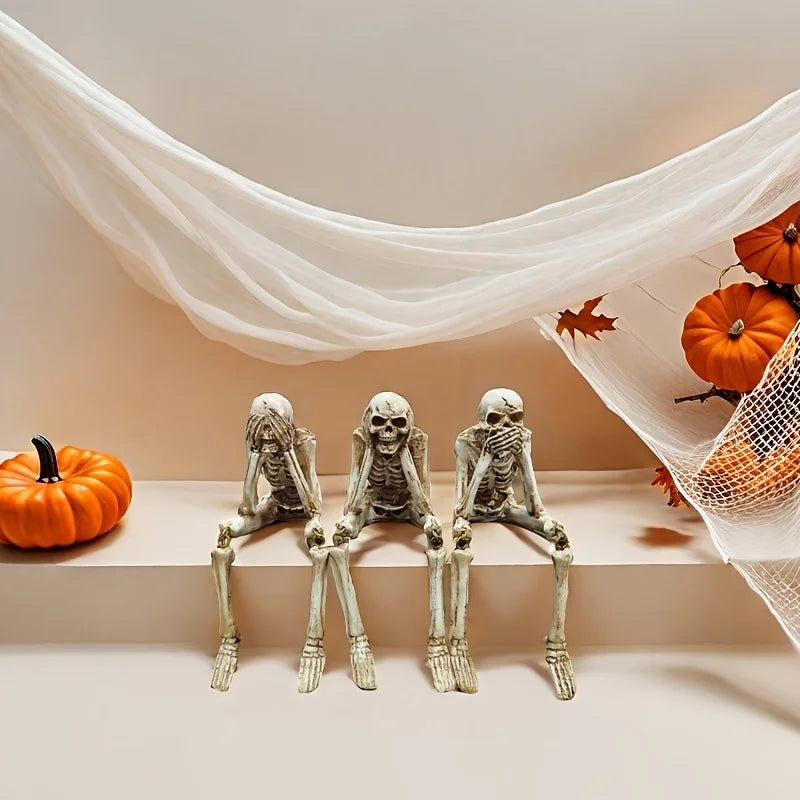 A set of realistic Halloween skeleton resin statues seated on a white shelf with sheer white fabric draped in the background.
