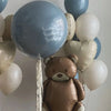 A cluster of foil balloons, including a brown teddy bear balloon and various light blue and white balloons.