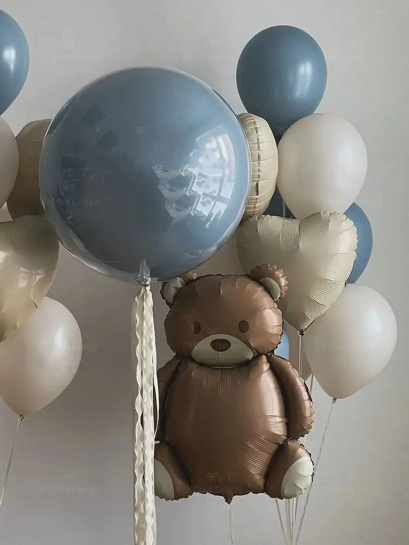 A cluster of foil balloons, including a brown teddy bear balloon and various light blue and white balloons.