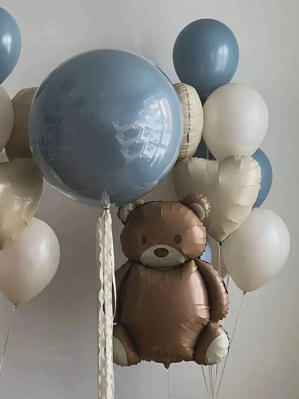 A cluster of foil balloons, including a brown teddy bear balloon and various light blue and white balloons.