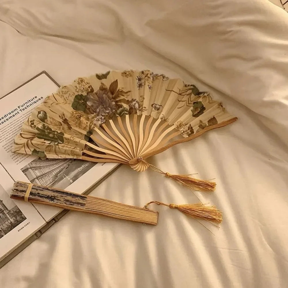 A beige and green leopard print folding hand fan with a black handle resting on a light-colored sheet.