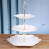 A three-tier gold cake stand with white ceramic plates for serving desserts and fruit.