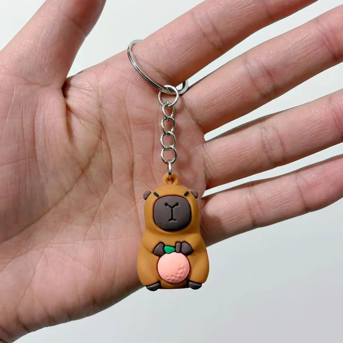 Pendentif de clé en argent d'une petite capybara brune ronde avec des accents roses.