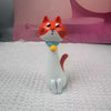 A white cat-shaped resin vase with orange ears and a blue collar is displayed on a white textured surface.