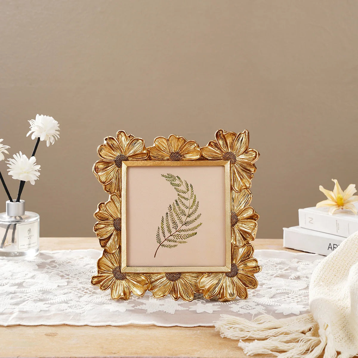 A golden 3D daisy resin photo frame with a natural green leaf inside, displayed on a white lace cloth.