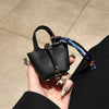 A hand holds a black mini house handbag with a multicolored wrist strap against a light background.