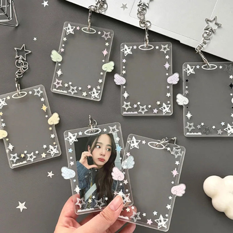 A hand holds an acrylic photocard holder keychain featuring a star pattern and small clouds on a gray background.