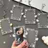 A hand holds an acrylic photocard holder keychain featuring a star pattern and small clouds on a gray background.
