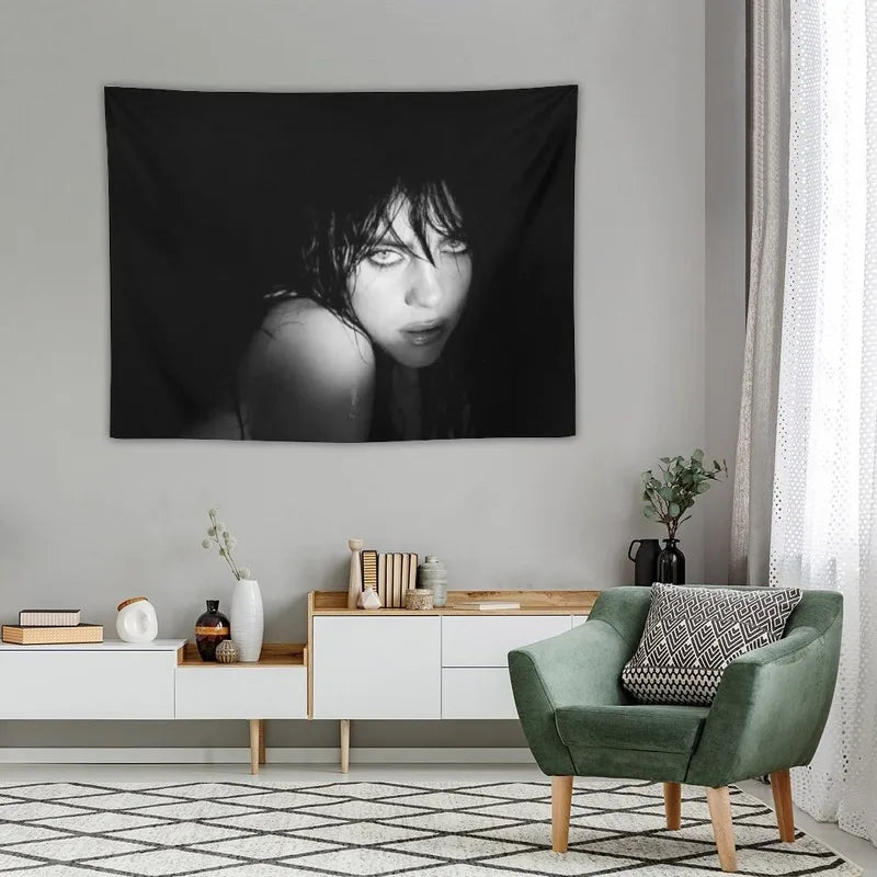 A black and white portrait of Billie Eilish as a tapestry wall hanging displayed on a light gray wall.