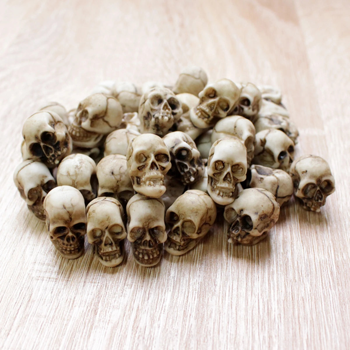 A collection of 20 realistic resin mini skulls used for garden decor, arranged on a light wooden surface.