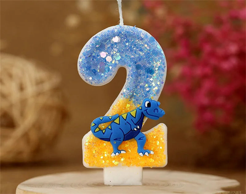 A birthday candle shaped like the number 2, decorated with blue glitter and a small dinosaur figure.