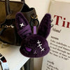 A dark purple gothic bunny plush keychain with a bandage design is displayed next to a black leather bag.