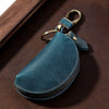 A dark teal Crazy Horse leather key pouch with a brass carabiner attached to a wooden surface.