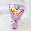 A bouquet of handmade crochet flowers in various pastel colors, including yellow, purple, and blue, presented in a lavender p