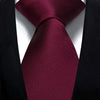 A close-up of a deep burgundy silk necktie tied in a simple knot against a black suit jacket.