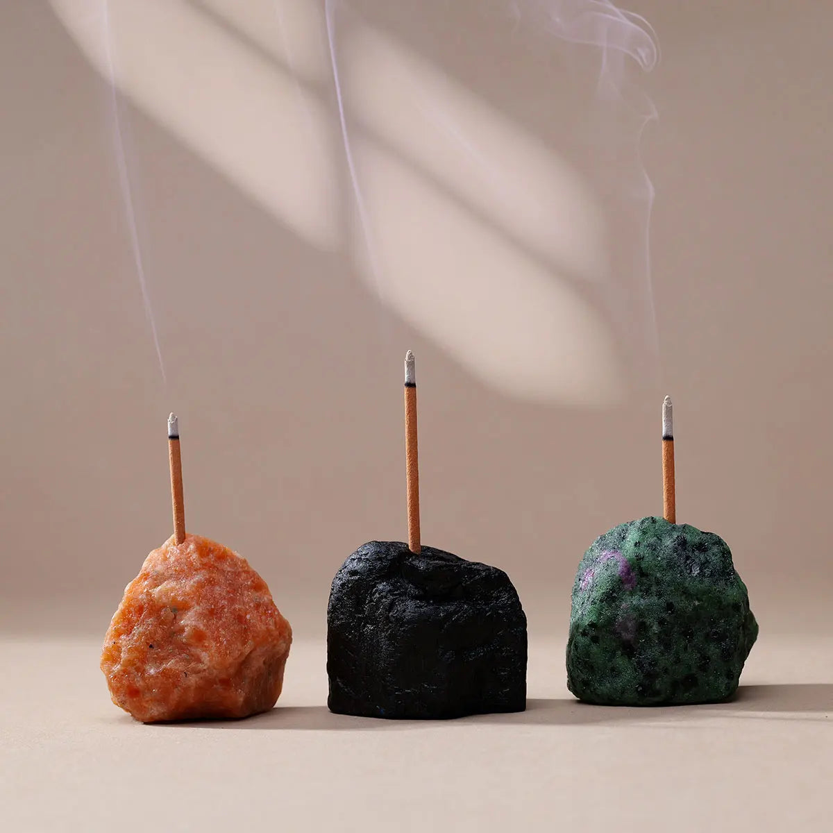 Three dark and colorful stones are shown with smoke rising from them, used as an aromatherapy holder.