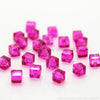 A collection of square cut pink glass crystal beads scattered on a white surface.