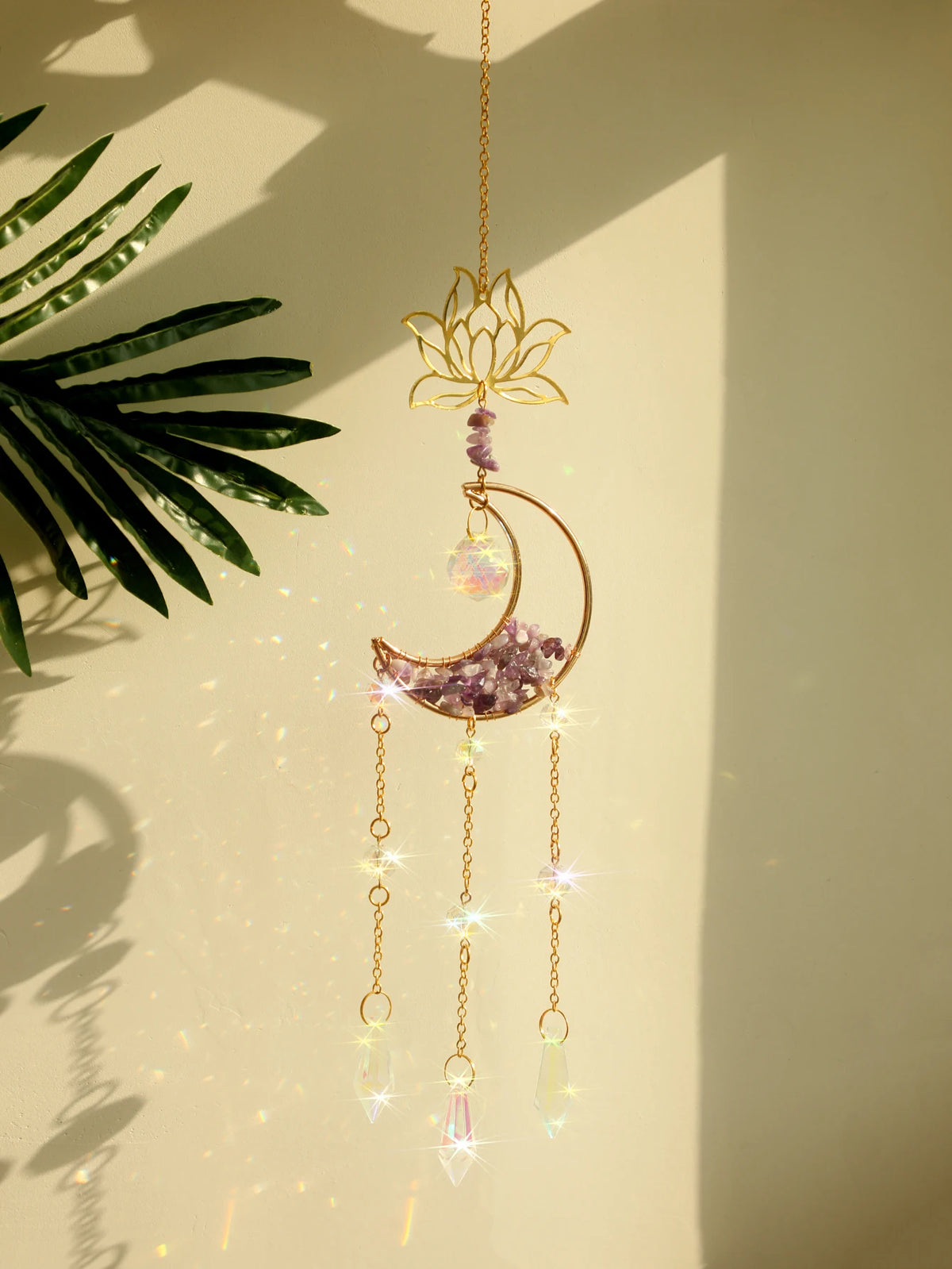 A handcrafted gold pendant featuring a lotus flower and a crescent moon made of purple crystal and clear glass beads.