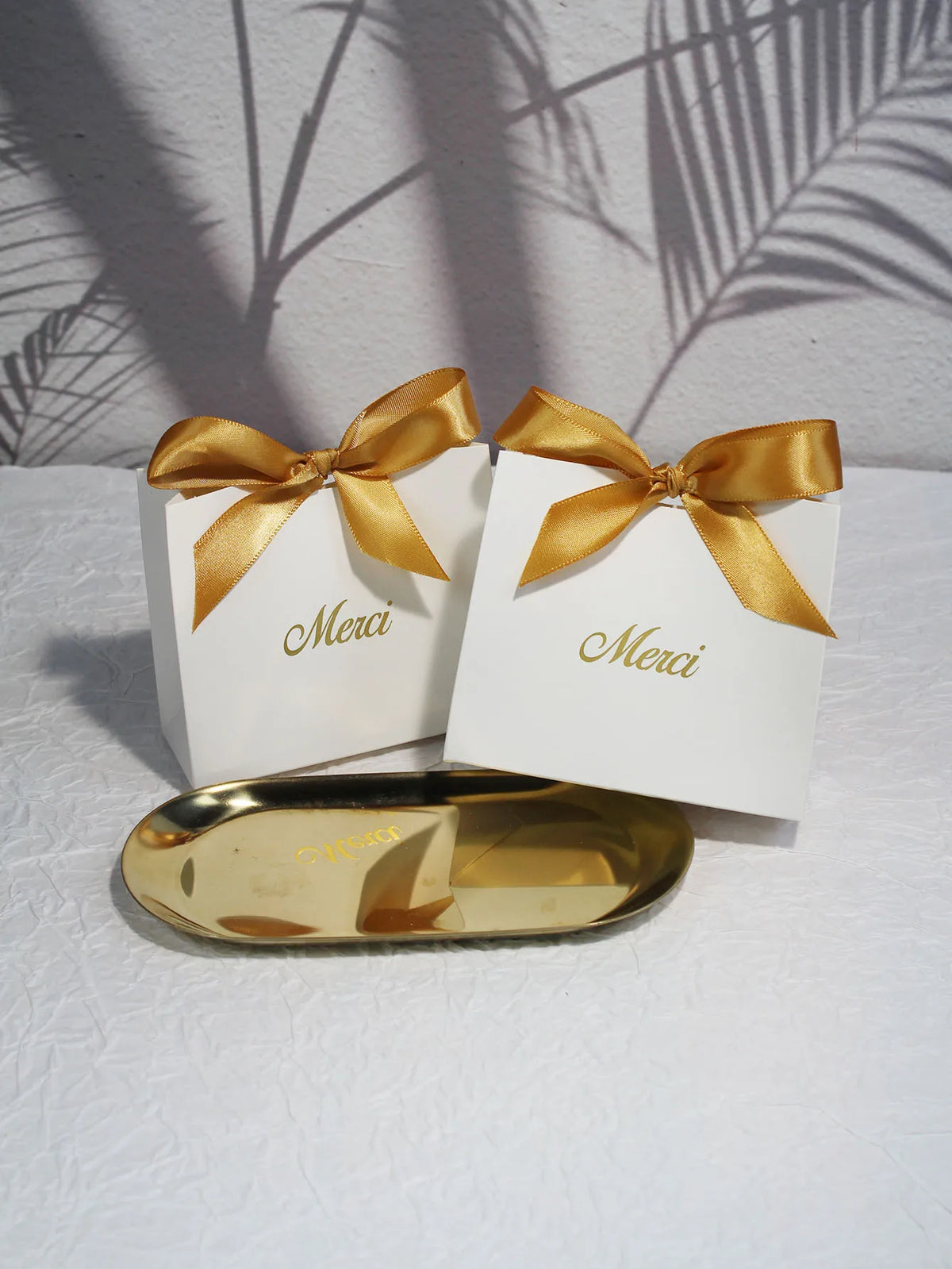 Two white thank you gift bags tied with gold ribbon resting on a gold tray.