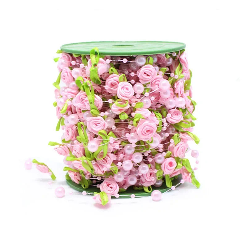 A cylindrical arrangement of pink roses, pearl beads, and green leaves used as a floral garland ribbon.