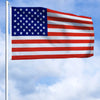 A large American flag waving on a flagpole against a blue sky.