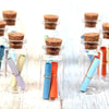 Glass cork stoppers with colorful wooden and plastic tubes displayed on a light blue background.