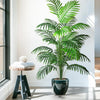 A realistic artificial palm tree with vibrant green silk leaves potted in a dark vase on a white floor.