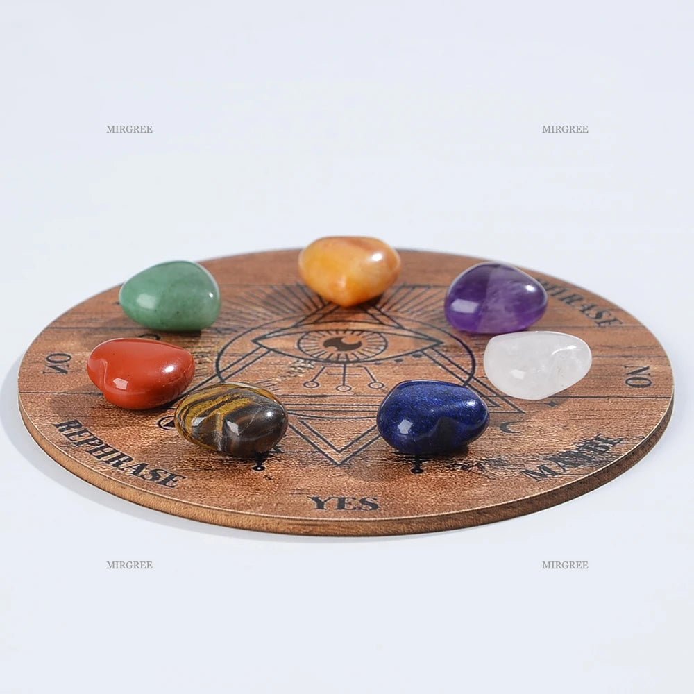 Un ensemble de sept cristaux polis, verts, jaunes, violets et bleus, disposés sur un plateau de divination en bois.