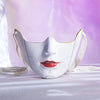 A white masquerade mask with a curved design and white fabric straps is displayed on a light surface against a purple backgro