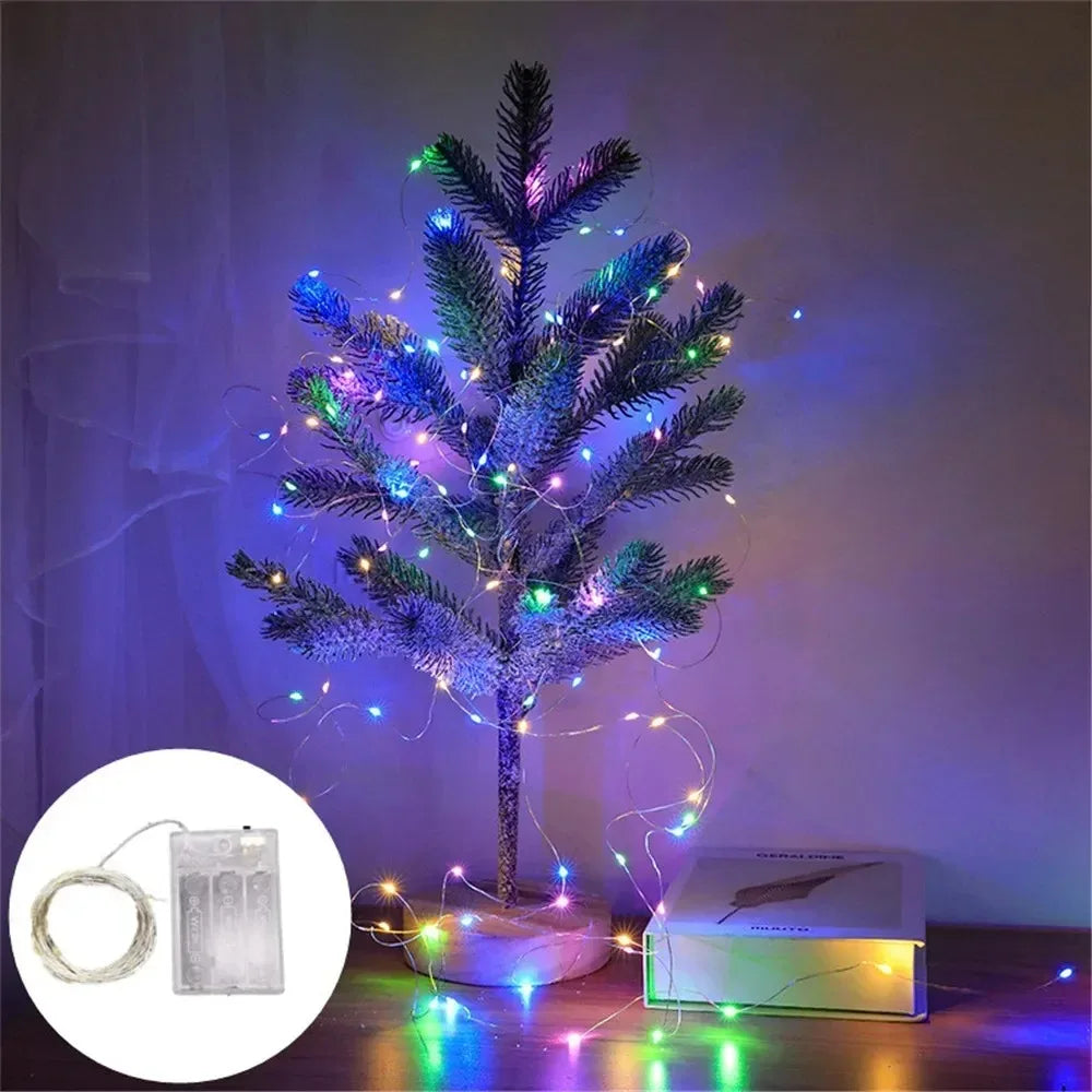 A decorated Christmas tree illuminated with blue and purple fairy string lights on a wooden surface.