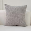 A gray linen pillow is displayed on a white surface.