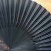 A close-up of a black folding hand fan with fine pleats and a bamboo frame, shown in a fan shape.