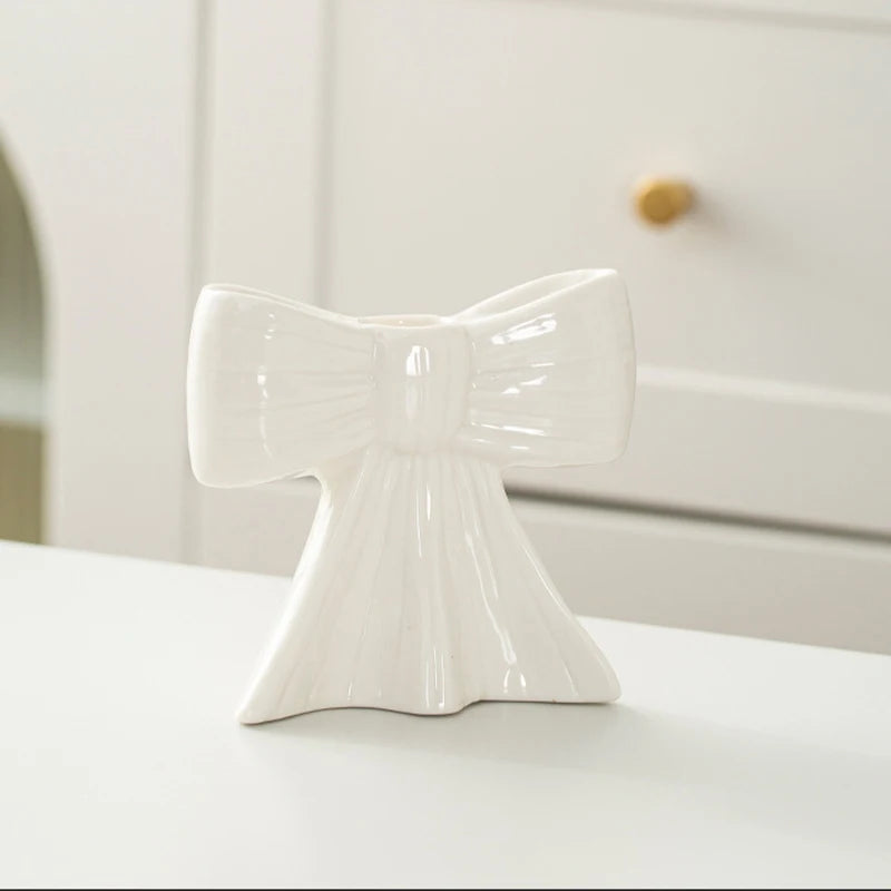 A white ceramic bow candle holder with a glossy finish sits on a white surface.