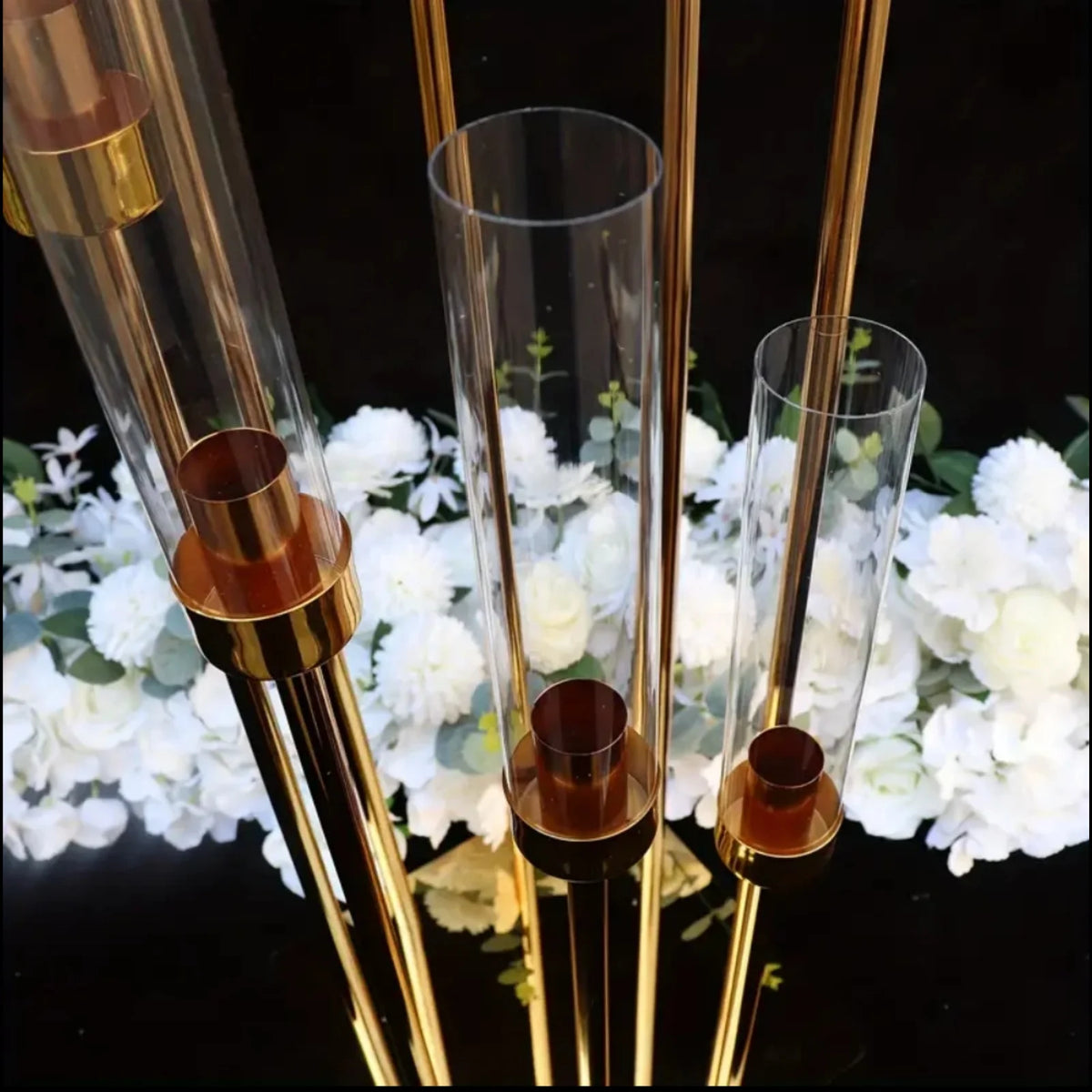 Elegant gold metal candle holders displayed with white flowers on a dark surface.