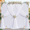 A white fabric backdrop decorated with draped curtains and floral greenery for an event.