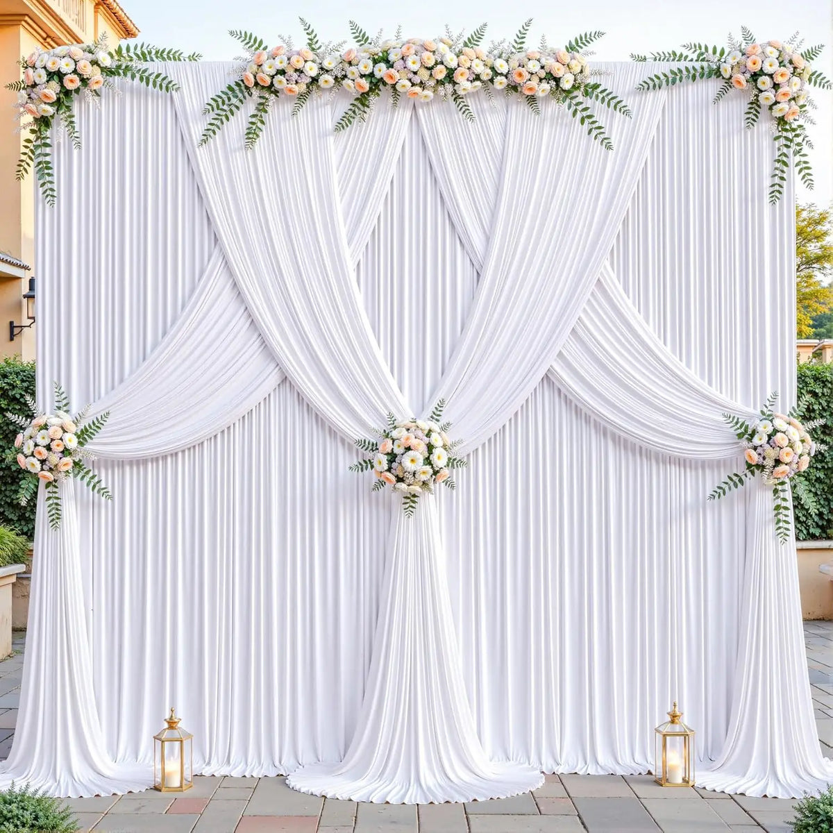 A white fabric backdrop decorated with draped curtains and floral greenery for an event.