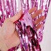 A hand holds a bundle of silver metallic foil fringe curtain material.