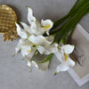 White artificial calla lily stems with yellow accents arranged on a gray surface.
