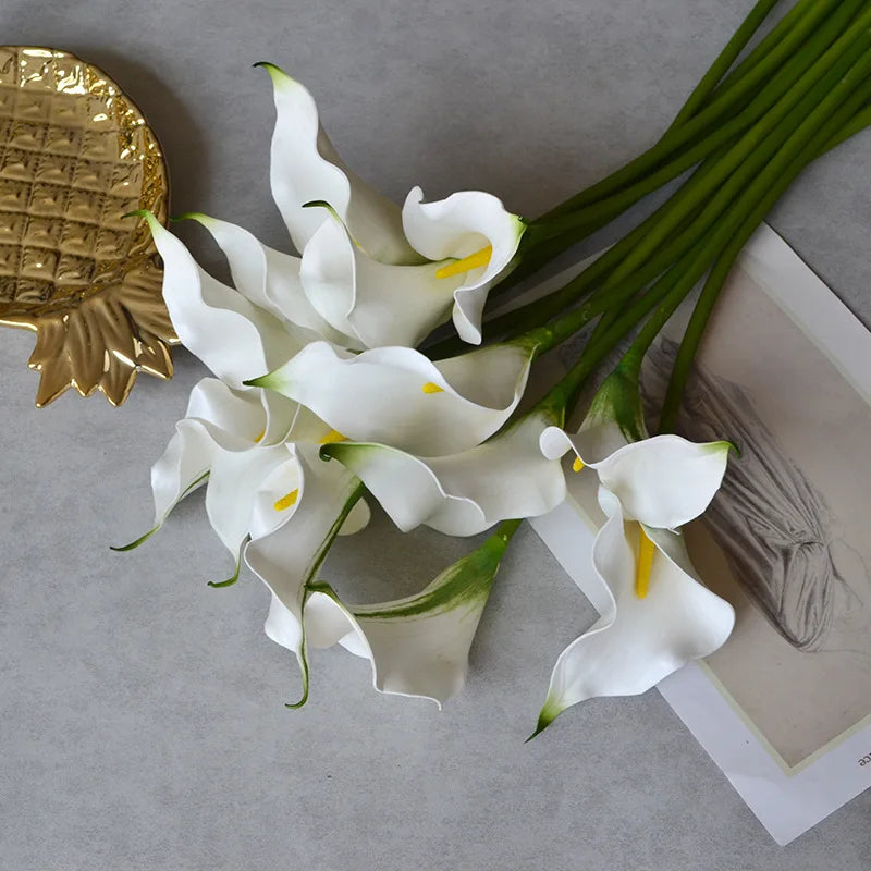 White artificial calla lily stems with yellow accents arranged on a gray surface.