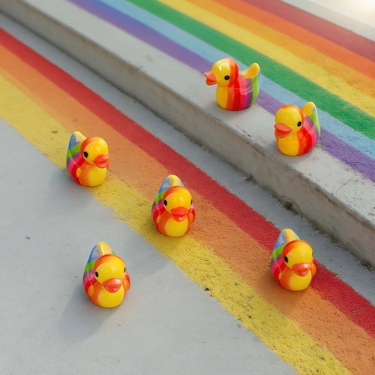 A set of small, colorful resin duck decorations arranged on a rainbow-colored surface.