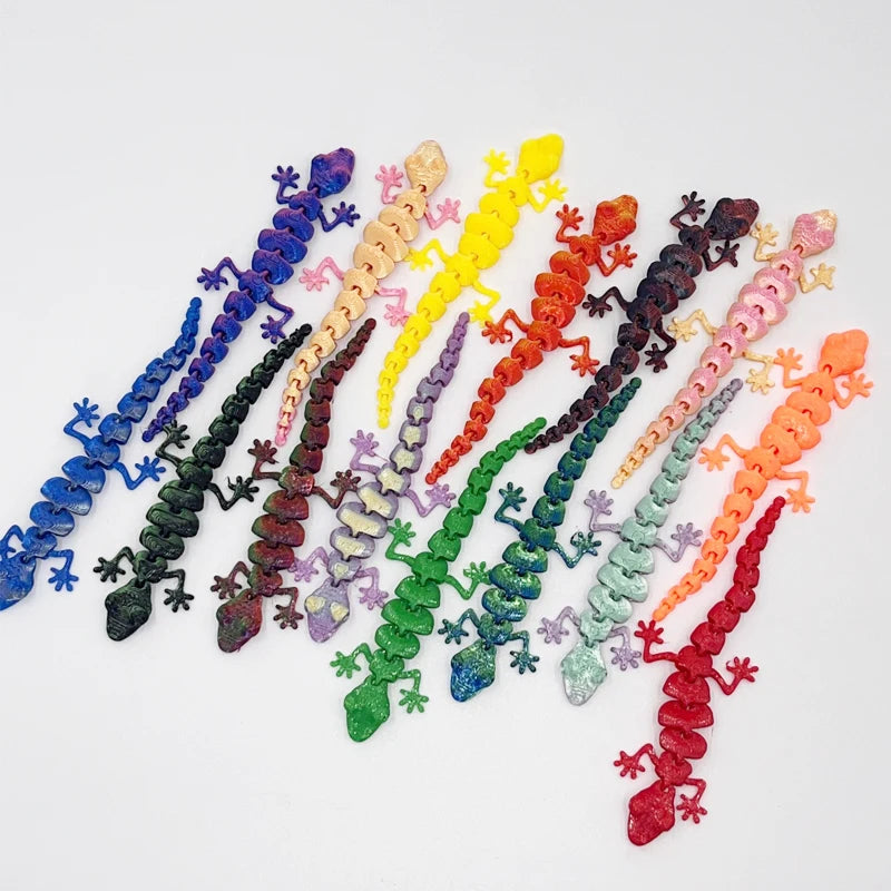 A collection of colorful 3D printed articulated gecko desk toys arranged in a line.